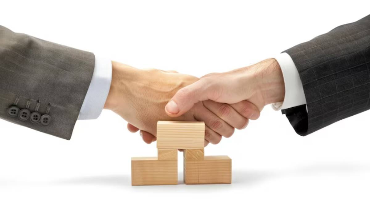 Two hands in business suits shake above wooden blocks, symbolizing a successful partnership or agreement.