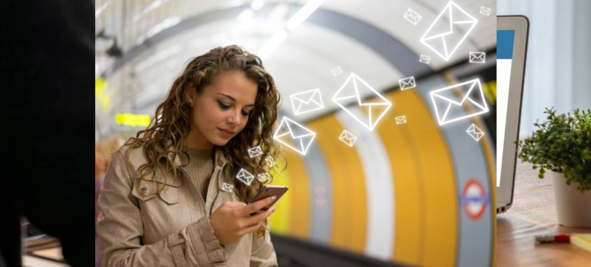 A person in a subway station holds a smartphone, surrounded by floating email icons, indicating communication or digital interaction.