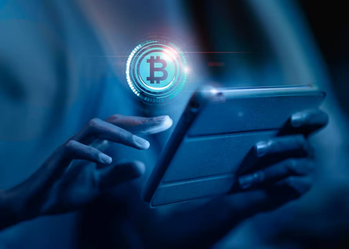 A person holds a tablet while interacting with a glowing Bitcoin symbol, set against a blue digital background.