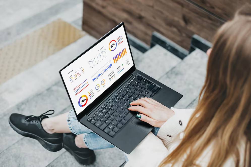 A person sitting on stairs, working on a laptop displaying colorful data visualizations and graphs.