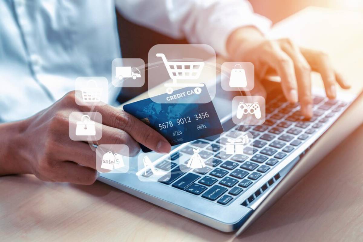 A hand holding a credit card near a laptop keyboard, overlaid with icons representing online shopping and security.