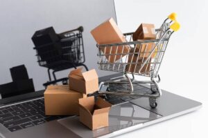 A miniature shopping cart filled with small boxes is placed on a laptop keyboard, symbolizing online shopping and e-commerce.