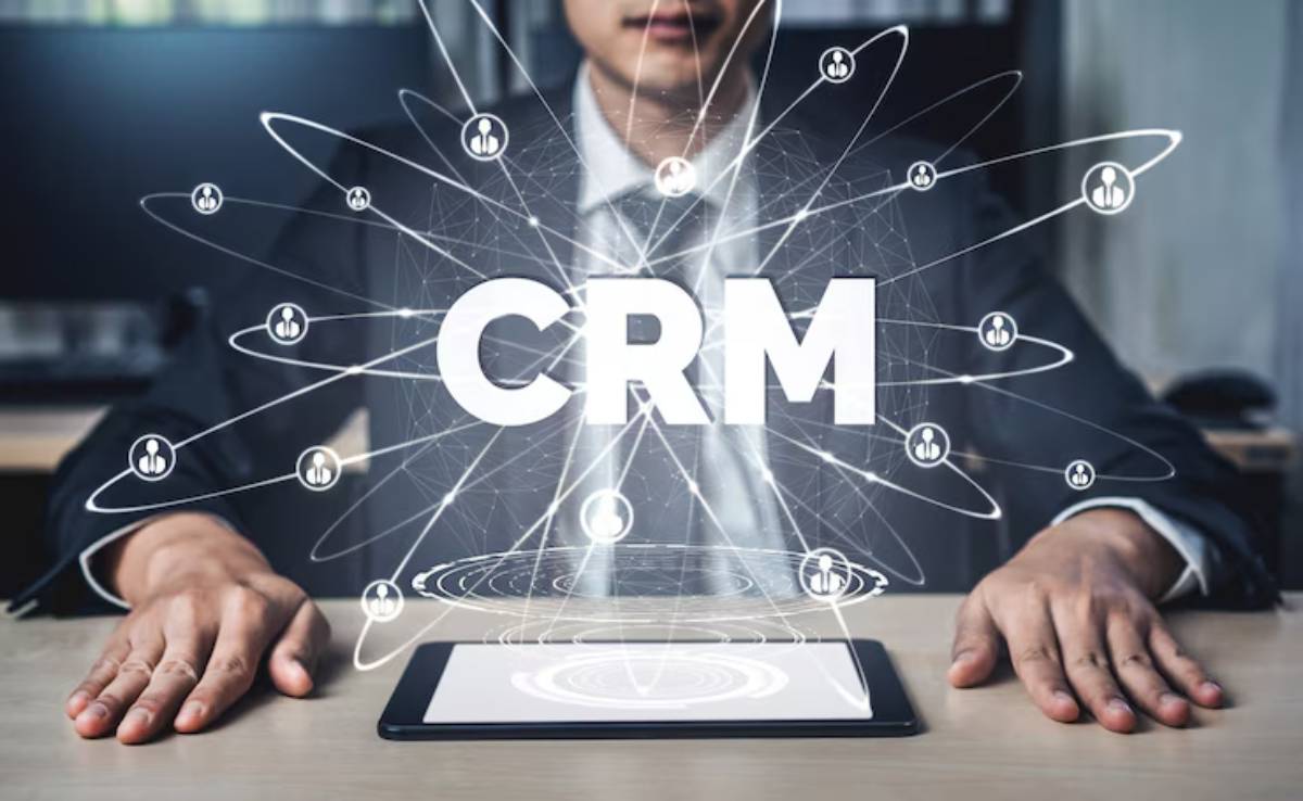 A businessman in a suit interacts with a tablet, surrounded by digital icons and the prominent text CRM representing customer management.