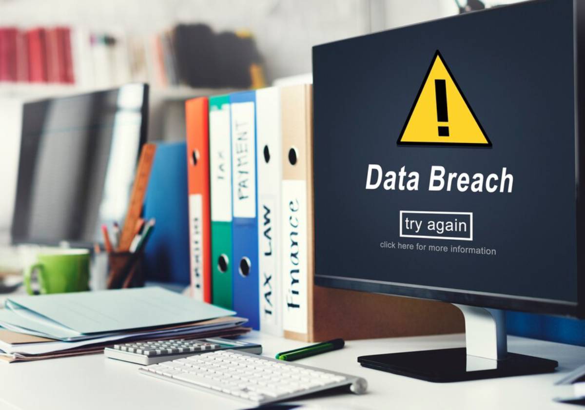A computer screen displays a warning about a data breach, alongside cluttered office supplies and colored file folders.