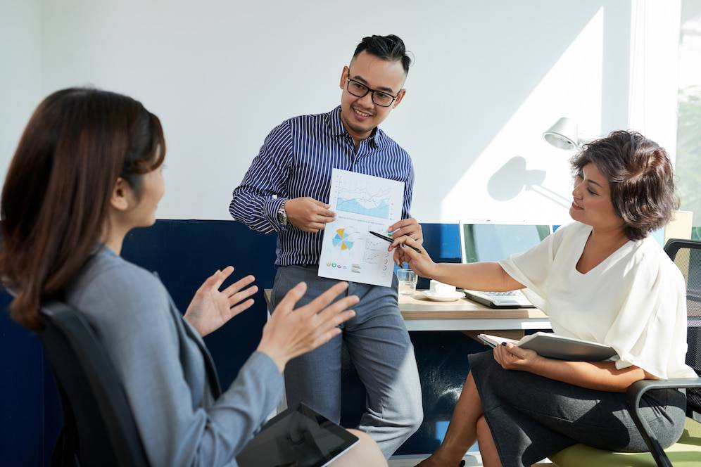 A group meeting in a modern office, with one person presenting charts while others engage actively in discussion.
