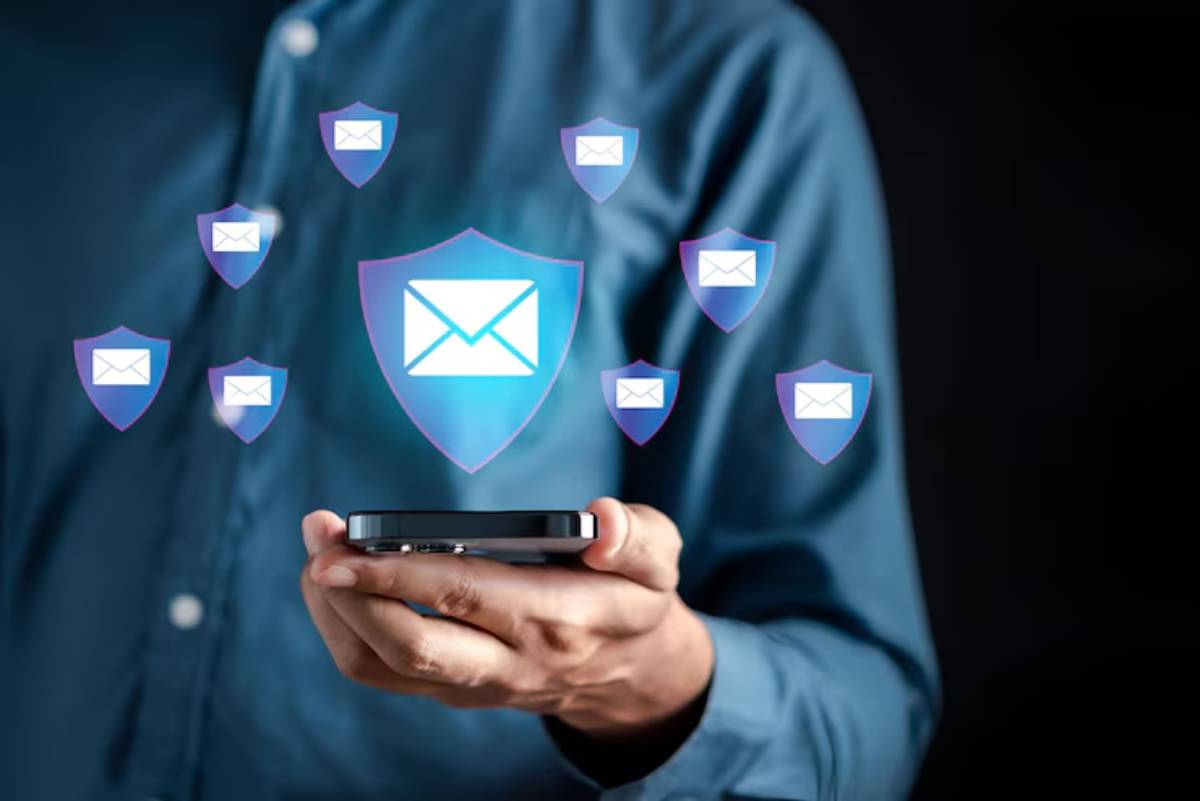 A person holds a smartphone with email icons and security shields floating above, symbolizing email protection and cybersecurity.
