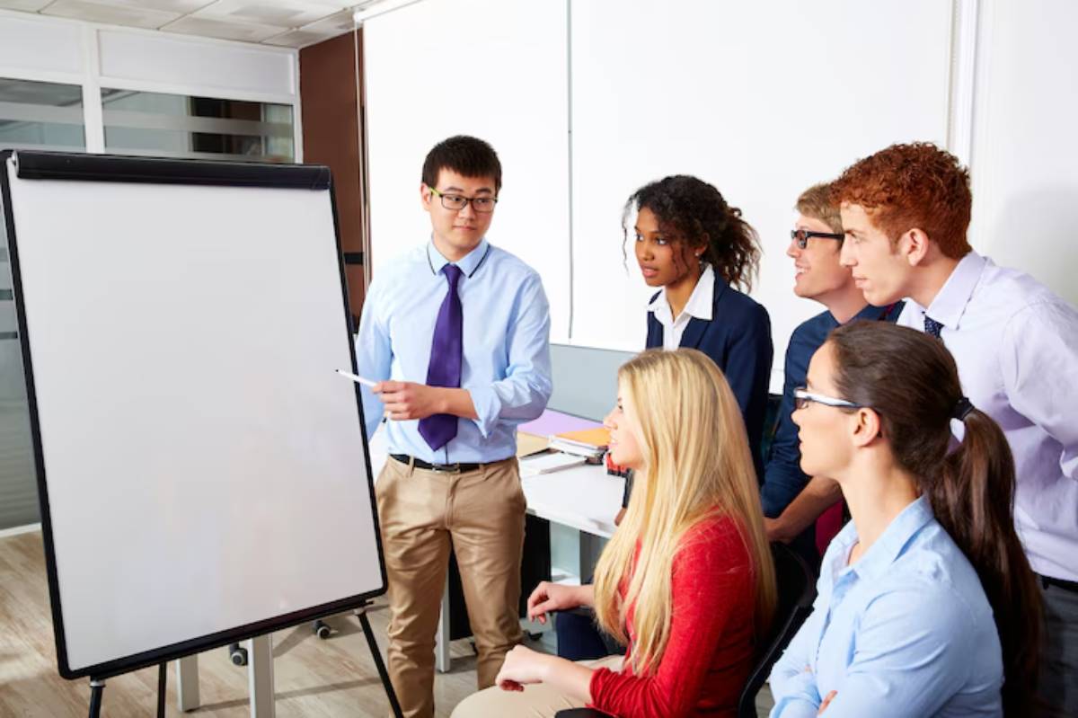 A group of professionals engages in a meeting, focusing on a presentation at a whiteboard in a modern office setting.