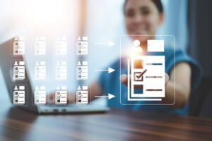 A person reaches out with an icon of a checklist, surrounded by multiple blurred images of similar profiles and a laptop on the table.