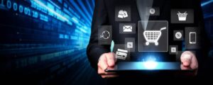 A businessman holds a tablet displaying various digital shopping icons, with a blue data background suggesting technology and commerce.