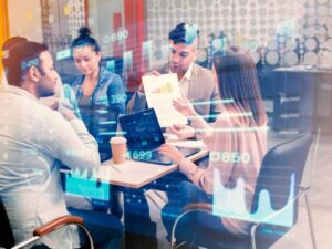 A group of professionals collaborate at a table, analyzing data on laptops while reviewing a report with graphics and statistics.