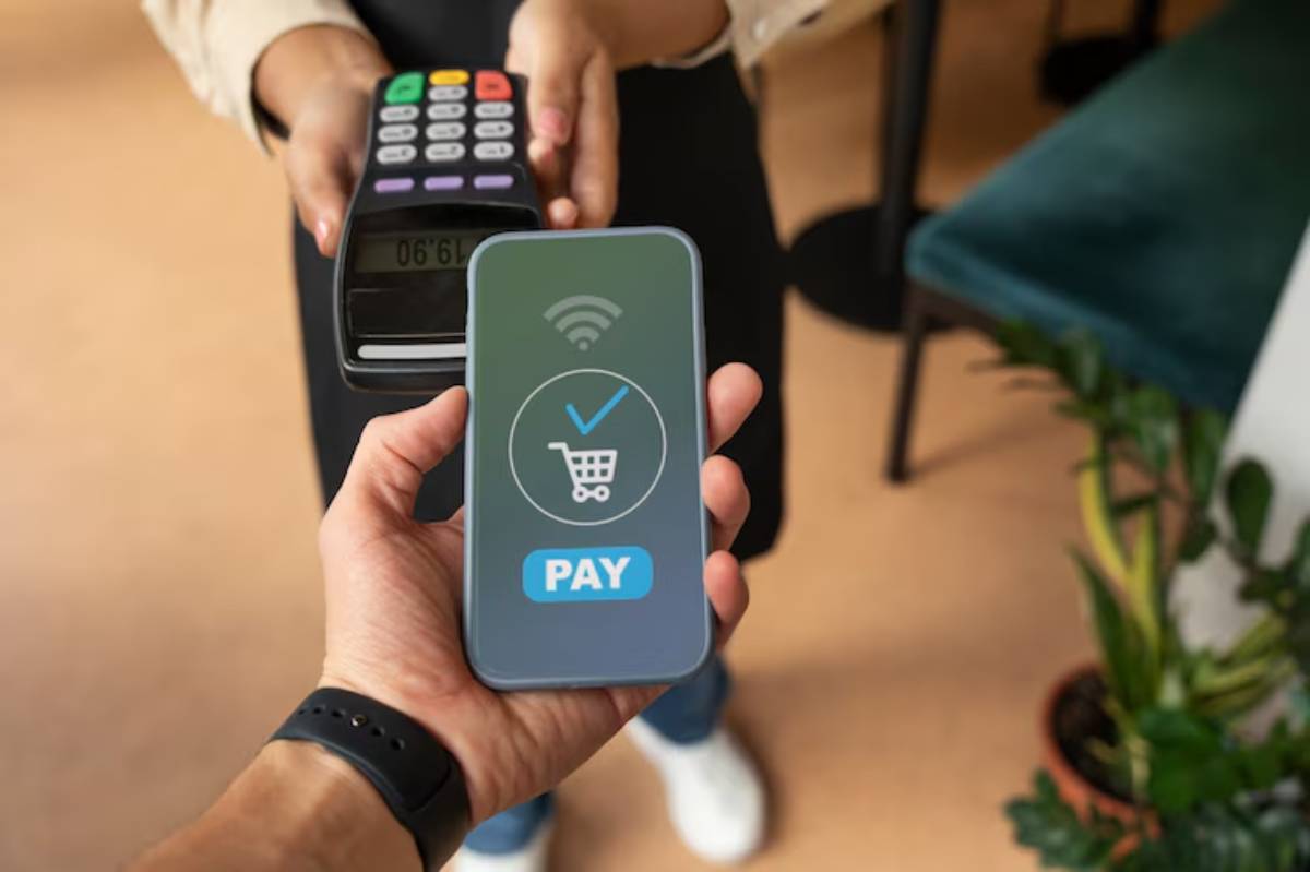 A close-up view of a person using mobile payment on their phone while holding it near a card terminal to complete a transaction.