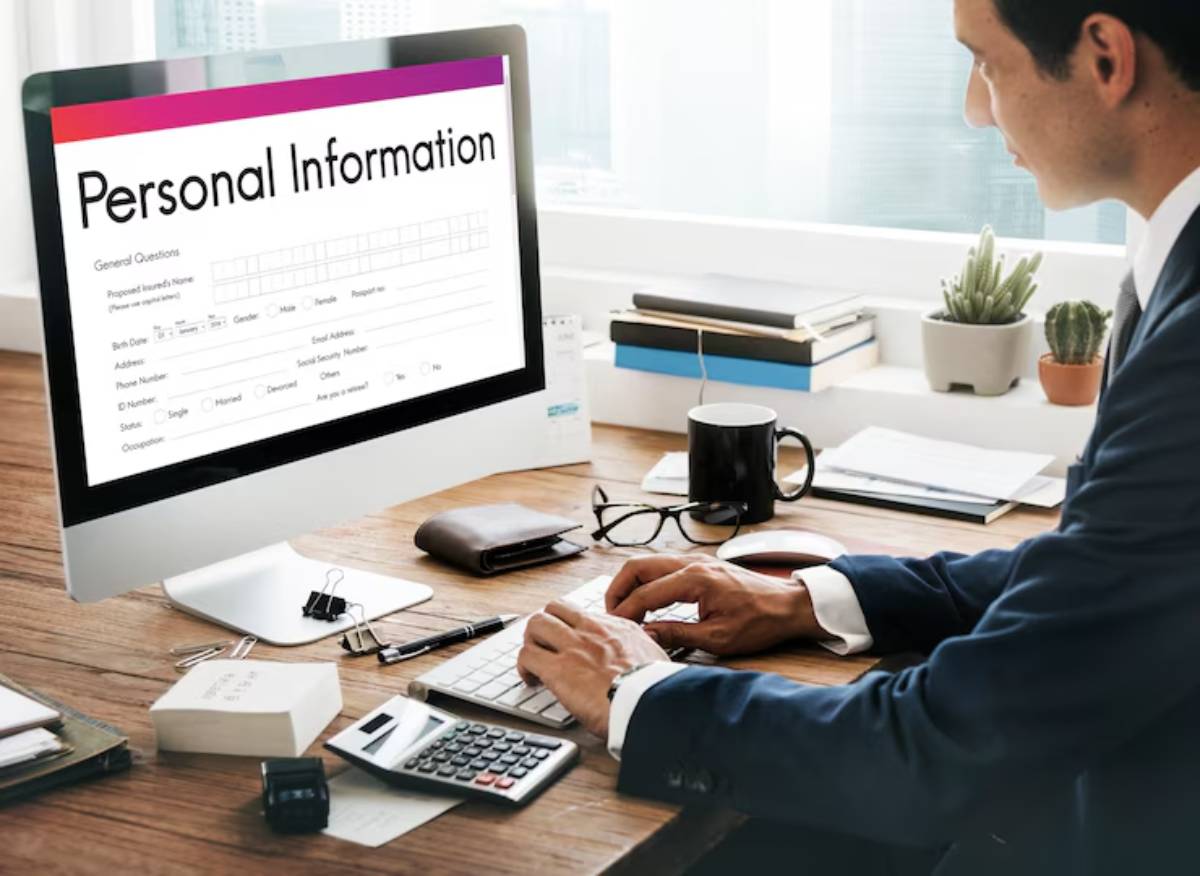 A professional at a desk is filling out personal information on a computer, surrounded by office supplies and a plant.