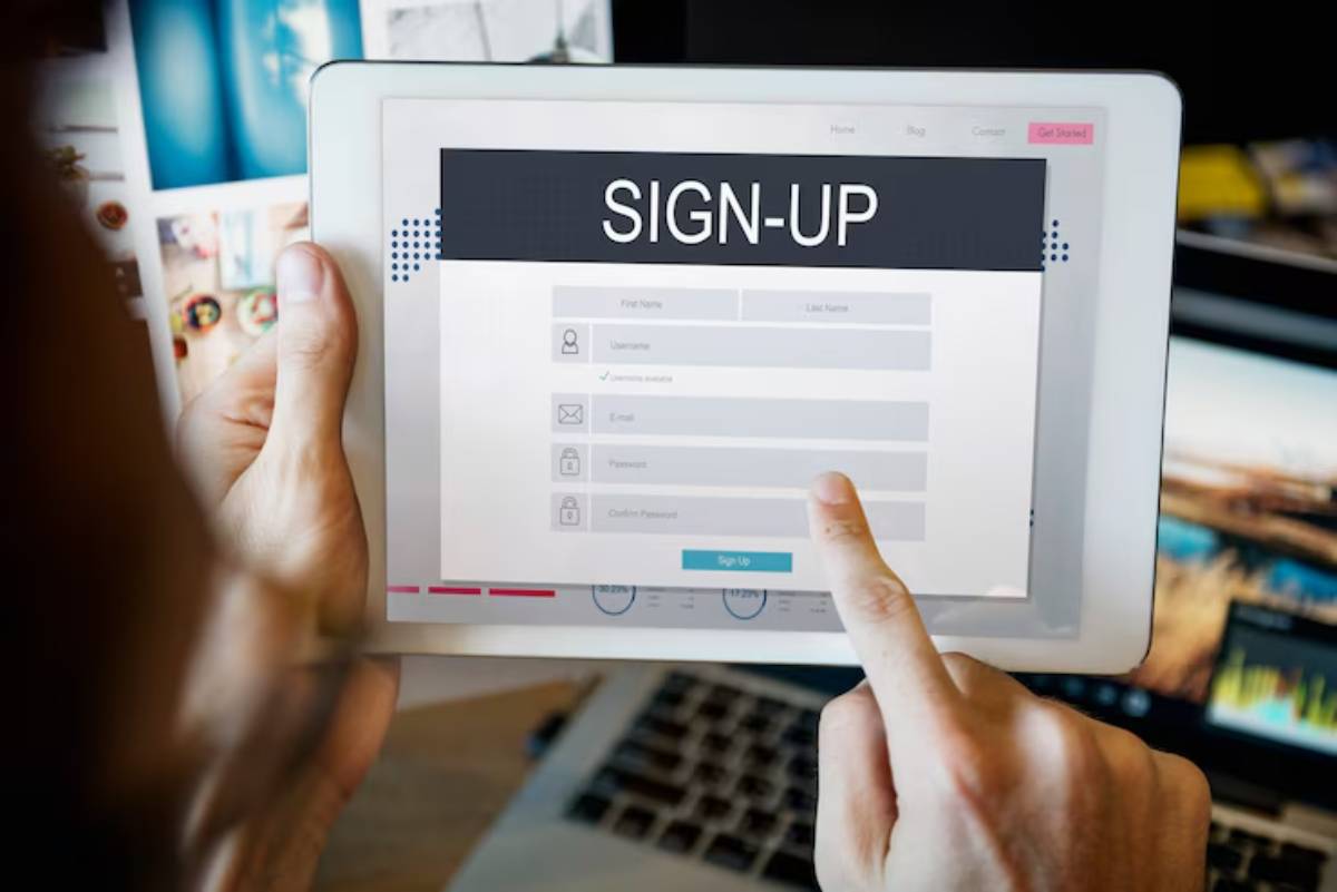 A hand points to a sign-up form on a tablet, displaying fields for personal information like name, email, and password.
