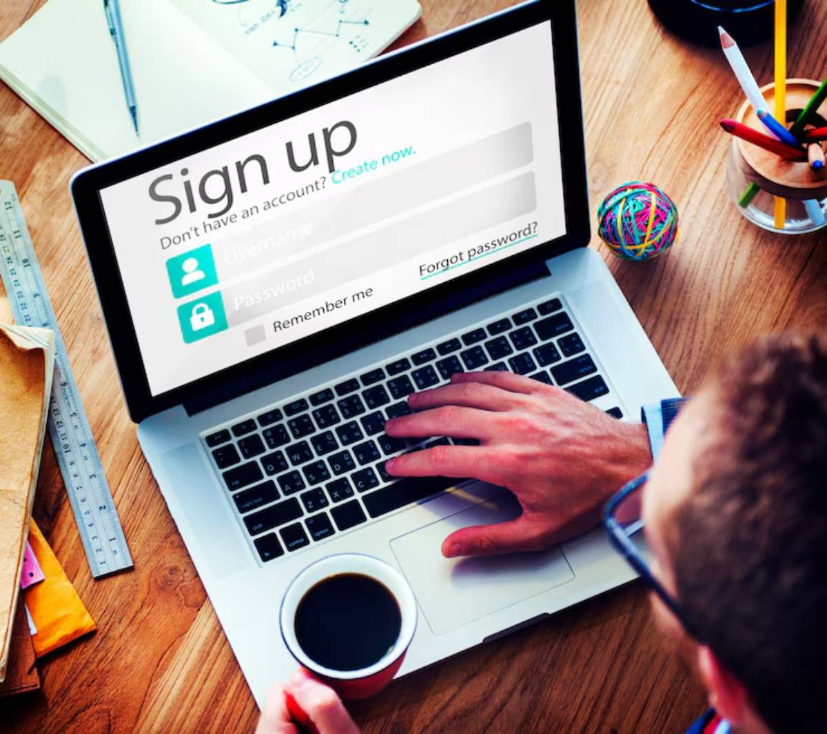 A person signing up on a laptop, with a Sign up screen displaying fields for username and password, alongside a coffee cup.