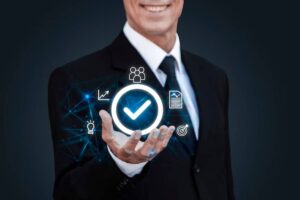 A smiling businessman in a suit holds a glowing checkmark, surrounded by icons representing teamwork, growth, ideas, and documents.